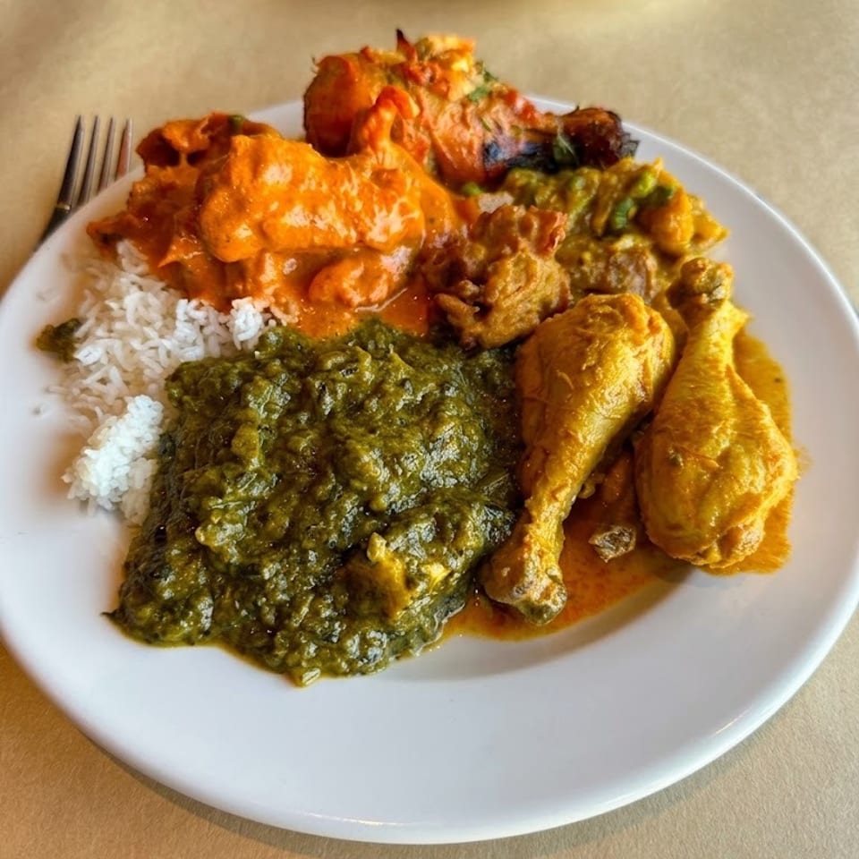 Plate of Indian cuisine featuring basmati rice, creamy orange curry, spinach curry, fried chicken, and naan on a restaurant table.