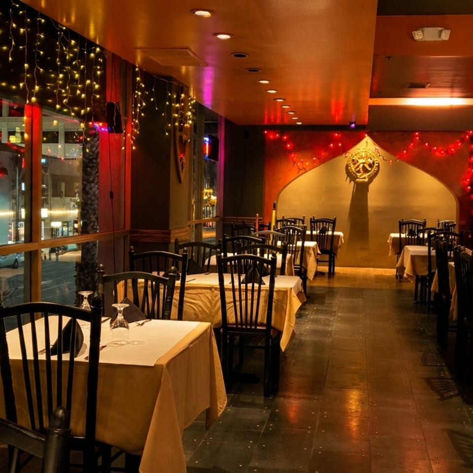 Elegant restaurant dining room with white tablecloths, black chairs, warm lighting, holiday string lights, and a decorated Christmas tree.